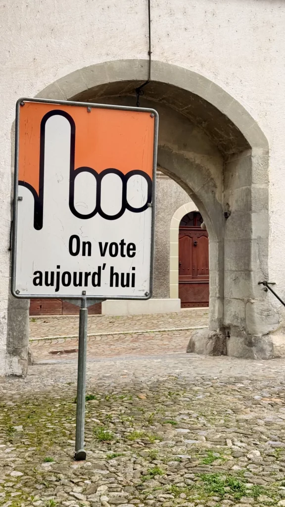Panneau « On vote aujourd’hui » devant une arche en pierre
